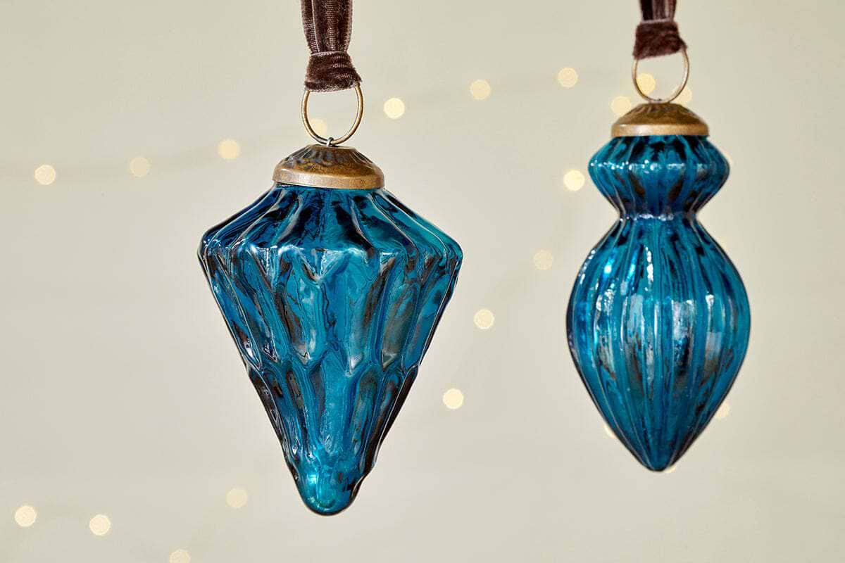 The nkuku Manipur Baubles - Indigo (Set of 3) feature elegant blue glass with gold accents and textured, geometric designs, hanging from brown ribbons—perfect vintage-style Christmas ornaments for festive decor.