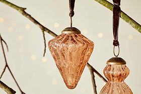 The Manipur Baubles - Copper (Set of 3) by nkuku feature textured, diamond-shaped glass with a brass top, hanging from a dark ribbon. Perfect for adding vintage charm and warmth to your festive decor.