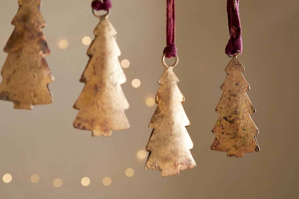 The nkuku Mishti Tree Baubles - Antique Brass (Set of 4, Small) feature a rustic gold finish and hang from maroon ribbons, creating a warm festive atmosphere with their antique charm.