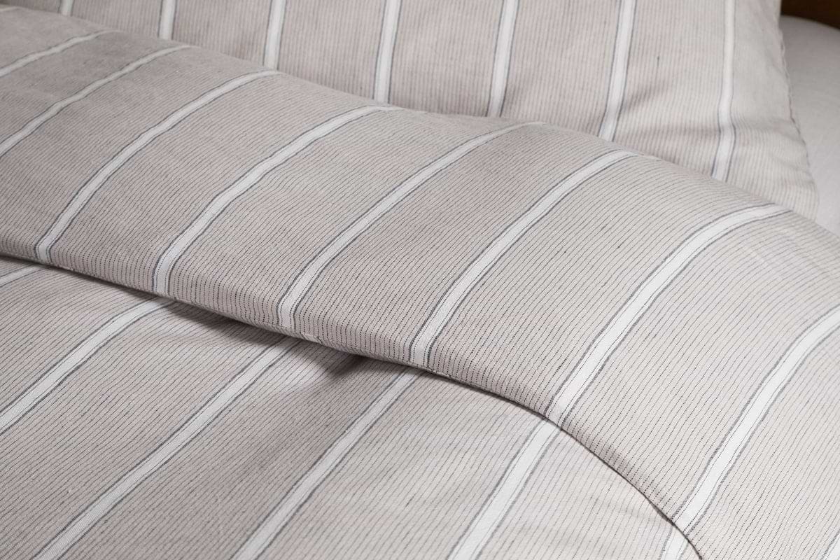 Close-up of a neatly made bed dressed in the Mora Hemp & Cotton Duvet Cover in Stone Grey by nkuku, showcasing soft, textured fabric for breathable comfort.