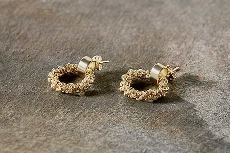 The Mula Earrings - Gold by nkuku are small, gold-plated hoops with a textured beaded design. Hypoallergenic, they feature round posts and circular studs for secure fastening and are shown resting on a rough stone surface.