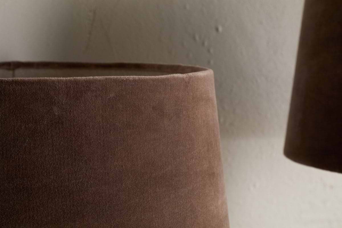 Close-up of the Mendai Velvet & Linen Lampshade in Mocha by nkuku, showing its soft brown velvet texture against a light, textured wall. The partial view highlights the smooth surface and neutral style.