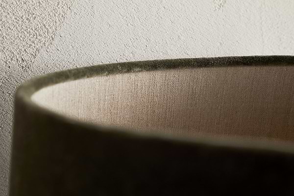 Close-up of the rim of the Mendai Velvet & Linen Lampshade in Moss Green by nkuku, showing its soft velvet curve, inner linen lining, and elegant decorative lighting details against a textured light-colored wall.