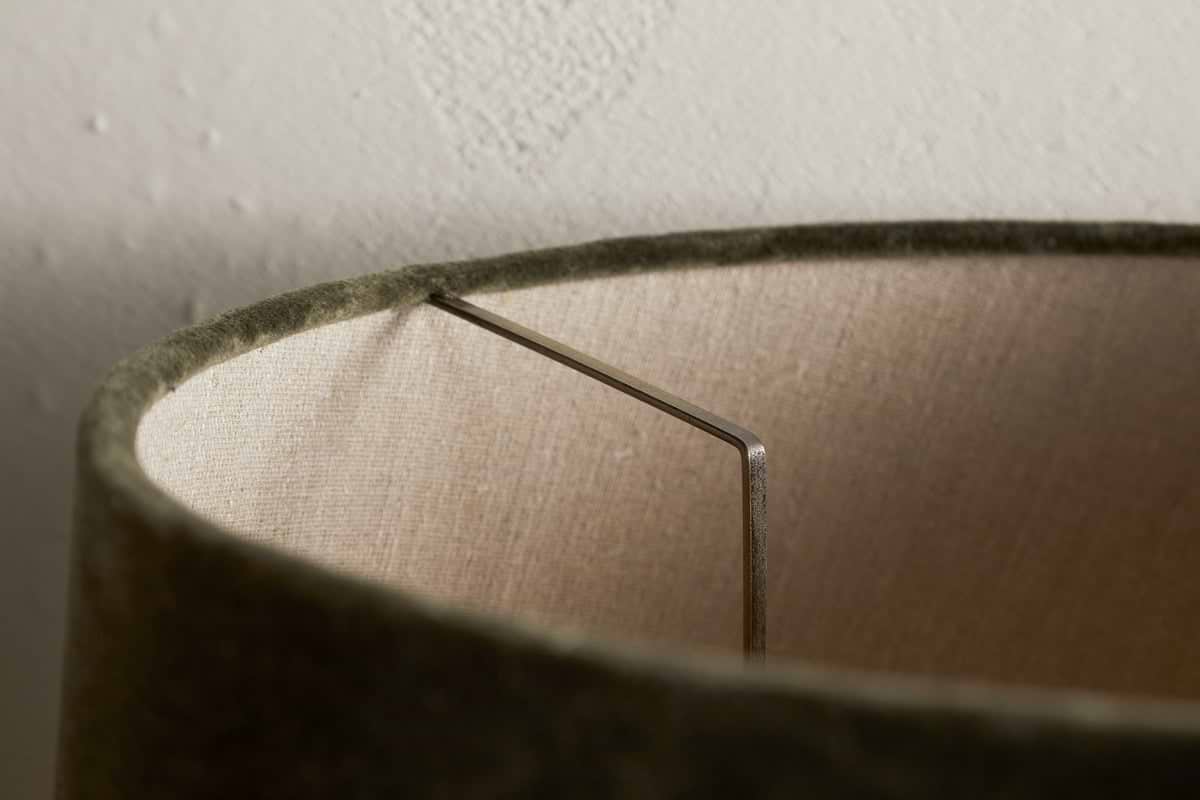 Close-up of the Mendai Velvet & Linen Lampshade by nkuku in Moss Green, highlighting its textured velvet exterior, beige linen interior, visible metal support, and a subtly stained white wall background.