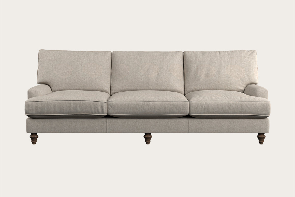 The Nkuku Marri Super Grand Sofa in Brera Linen Natural features a generous three-seat design with plush back and seat cushions, gently angled armrests, and elegant dark wooden turned legs, set against a plain light background. Its handcrafted linen upholstery boasts a soft, textured feel that enhances the sofa's classic and comfortable appearance—a testament to fine craftsmanship inspired by Nkuku’s Nottinghamshire workshop.