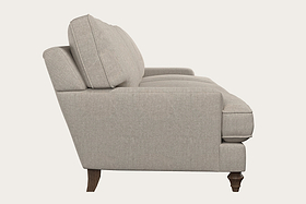 A side view of the Marri Super Grand Sofa - Brera Linen Natural by Nkuku, featuring light beige handcrafted linen upholstery, plush cushions, a straight back, rounded armrests, and dark wooden legs—expertly crafted in a Nottinghamshire workshop—shown against a plain off-white background.