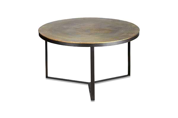 The nkuku Maba Coffee Table features a round, antique brass top with a rustic finish and three slim black metal legs in a triangular base—ideal as a characterful coffee table for your living room. Plain white background.