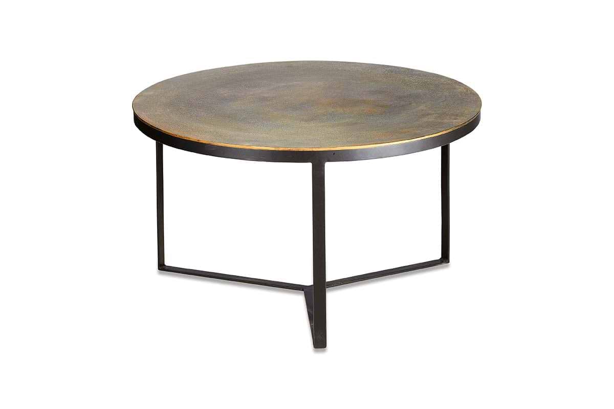 The nkuku Maba Coffee Table features a round, antique brass top with a rustic finish and three slim black metal legs in a triangular base—ideal as a characterful coffee table for your living room. Plain white background.