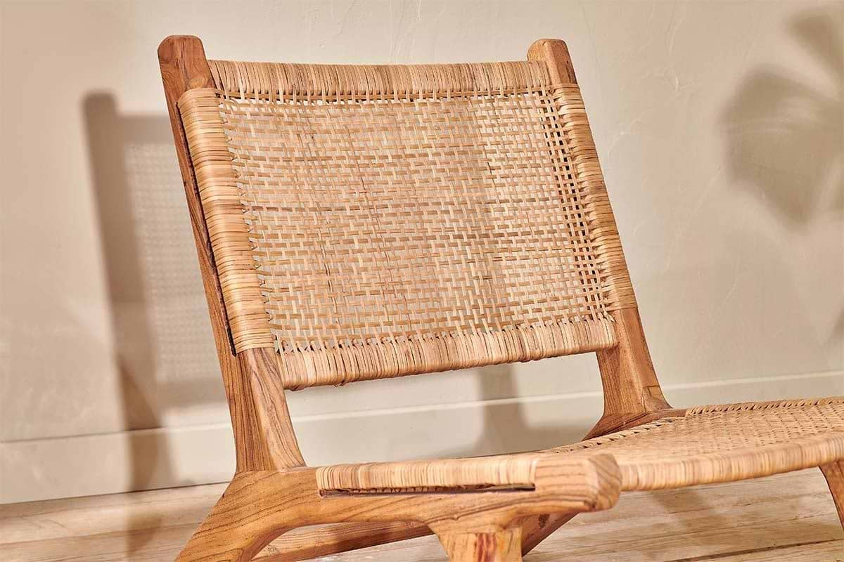 Close-up of the Madrisana Acacia & Rattan Woven Chair by nkuku, a low-seated design featuring natural acacia wood and a woven rattan seat and back, with light accentuating the unique textures.