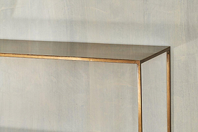 A close-up shows the top edge of the Mahi Console Table by nkuku, featuring a gold frame and set against a light gray, textured wall.