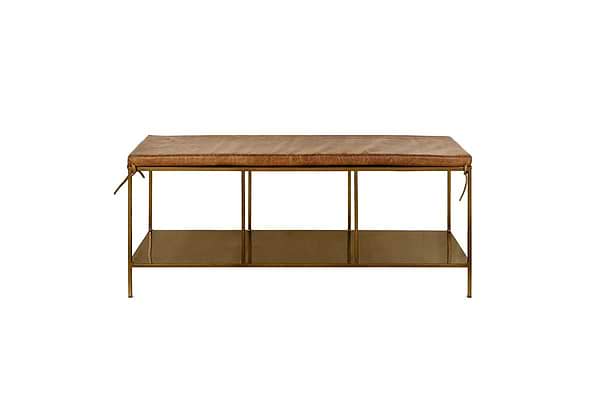 The nkuku Mahi Iron & Leather Bench features a rectangular tan leather cushion with side ties, slender brass legs, and a metal lower shelf. This minimalist bench is photographed against a plain white background.