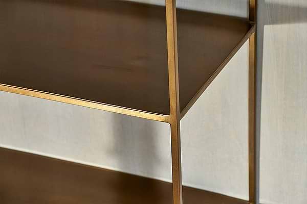 Close-up of the nkuku Mahi Shelving Unit - Wide in matte gold, highlighting where the shelves join the vertical frame. This minimalist brass unit brings modern style and clean lines to any subtly textured light gray wall—ideal for elegant storage.