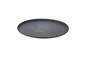 The Mahika Tray - Black by nkuku is a round, shallow aluminium tray with a black finish, raised edge, and hand-etched circular dotted pattern radiating from the center, shown on a plain white background.
