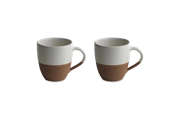 Two nkuku Mali White & Terracotta ceramic mugs with handles are shown side by side, each with an off-white glazed upper half and unglazed terracotta base, creating a minimalist two-tone look against a plain white background.