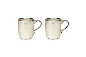 The nkuku Malia Mug - Cream (Set of 2) features a textured rim, dark brown accents, and a stunning reactive glaze, shown side-by-side on a white background.