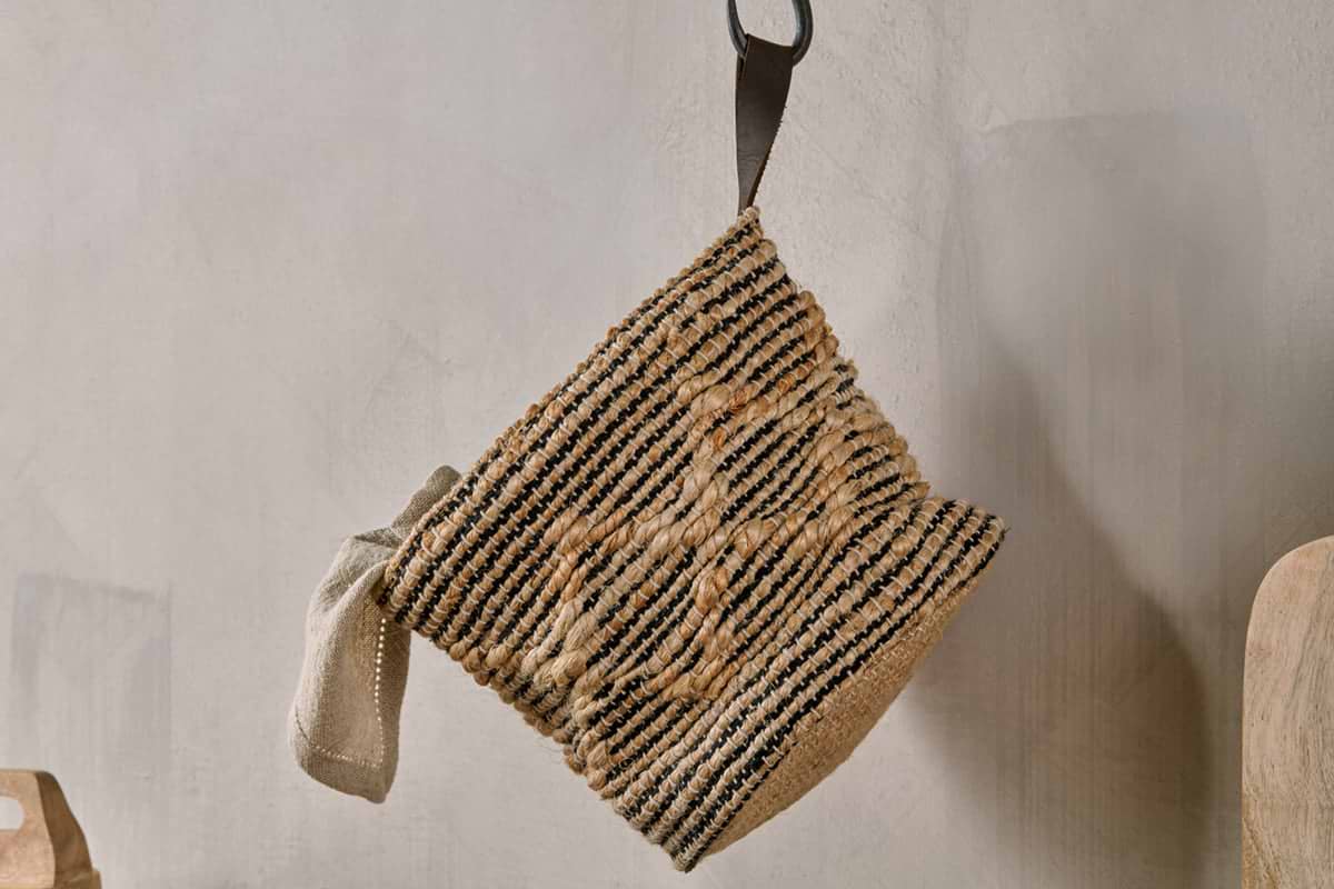 The Mannu Cotton & Hemp Wall Hung Basket by nkuku, in natural and black stripes with a central star design and hanging loop, is ideal for adding artisan style to any cozy kitchen or dining area.