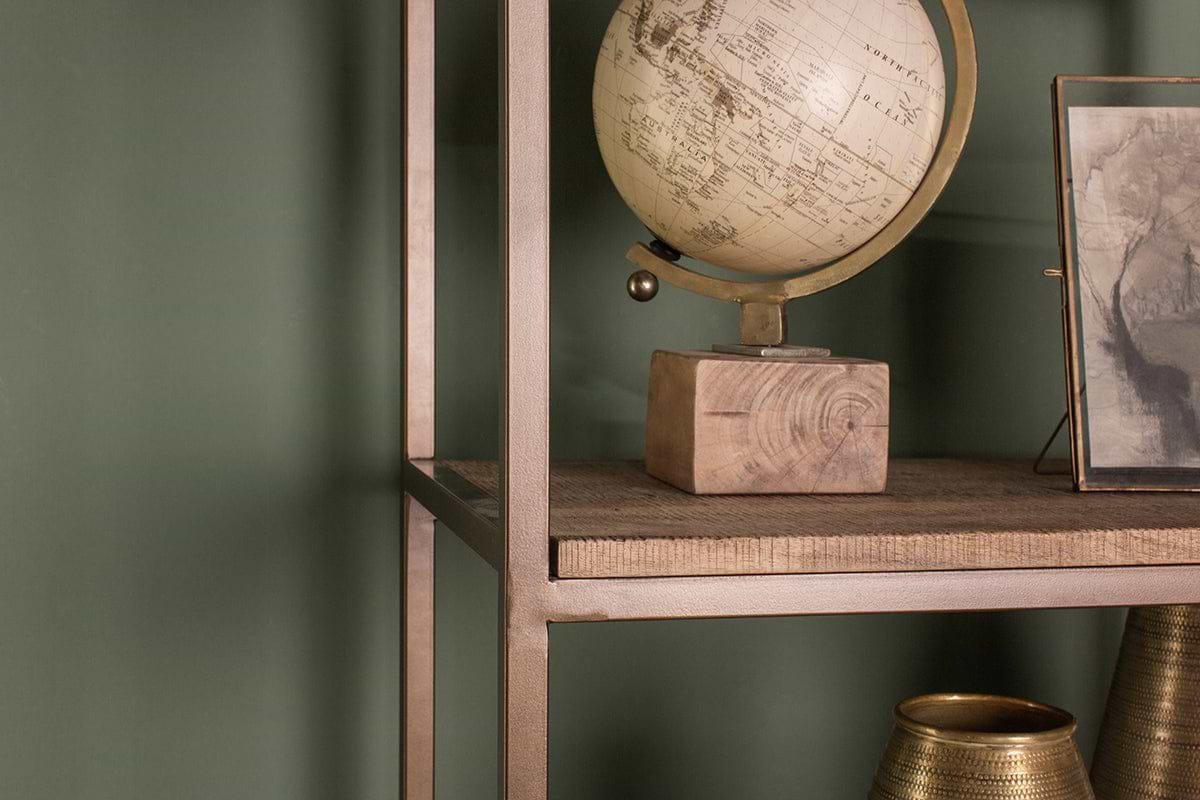 A close-up of the nkuku Marjori Mango Wood And Iron Standing Shelves - Wide against a green wall, styled with a vintage globe on a wooden base, a framed picture, and two metallic vases (one partly visible in the bottom right).