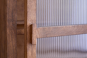 Close-up of the Mendani Mango Wood & Fluted Glass Low Cabinet by nkuku, featuring a walnut-stained finish, vertical handle, and fluted glass panel in a wooden frame that highlights the wood grain, joinery, and detailed craftsmanship.