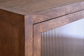Close-up of the Mendani Mango Wood & Fluted Glass Low Cabinet by nkuku, showing vertical fluted glass on the door, reflecting light and contrasting with the warm walnut-stained finish for a modern, minimalist look.