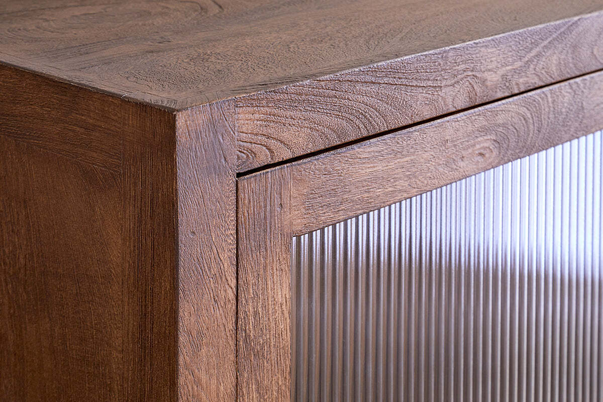 Close-up of the Mendani Mango Wood & Fluted Glass Low Cabinet by nkuku, showing vertical fluted glass on the door, reflecting light and contrasting with the warm walnut-stained finish for a modern, minimalist look.