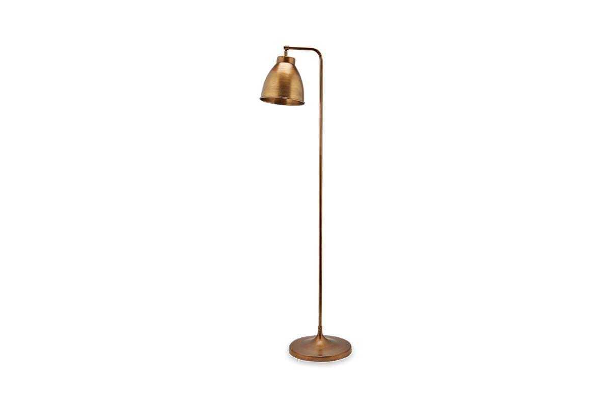 The nkuku Muturi Floor Lamp - Antique Brass features a tall, slender solid brass frame with an angled stem and round base. Its conical shade offers stylish down lighting, bringing modern elegance to any space.