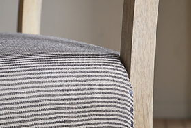 Close-up of the nkuku Nadeeka Linen Upholstered Counter Chair in soft grey, featuring textured striped linen and a light wood frame—ideal for your kitchen island.
