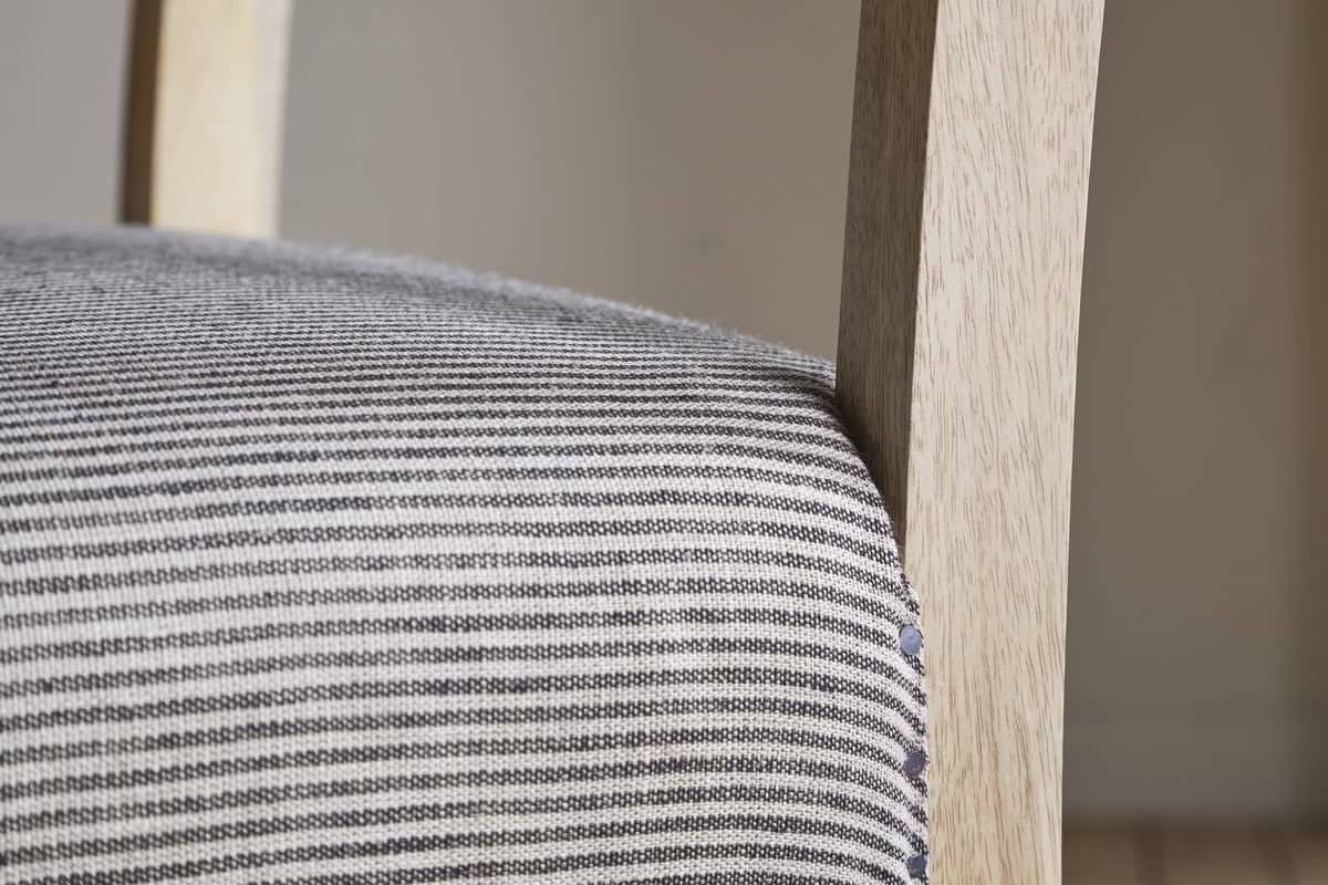 Close-up of the nkuku Nadeeka Linen Upholstered Counter Chair in soft grey, featuring textured striped linen and a light wood frame—ideal for your kitchen island.