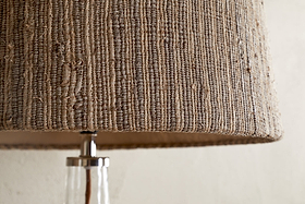 Close-up of the nkuku Nadee Banana Leaf Lampshade in Natural, featuring its textured, woven surface made from sustainable banana leaf fibers. Below, part of a clear glass base with a metallic fitting is visible.