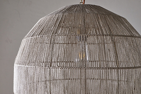 Close-up of the Nilaveli Woven Jute Sphere Pendant by nkuku, featuring a textured natural jute dome lampshade. Soft light glows through the woven strands, set against a plain, neutral background.