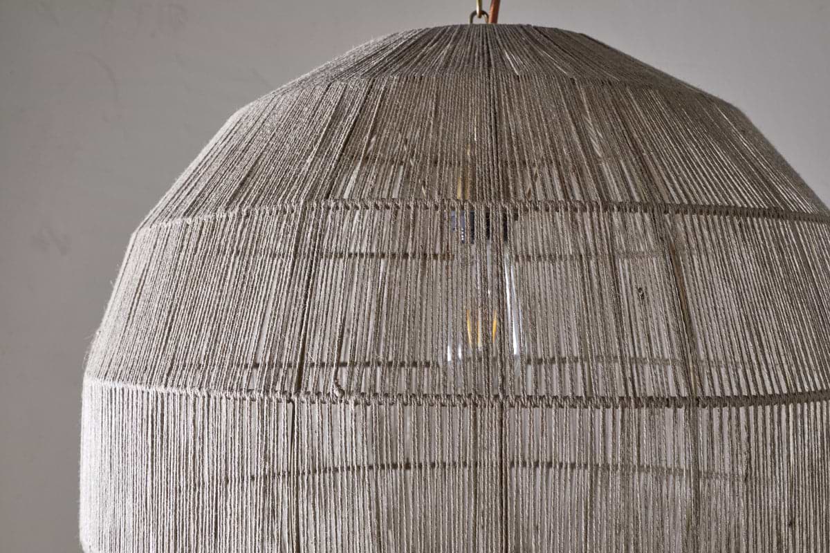 Close-up of the Nilaveli Woven Jute Sphere Pendant by nkuku, featuring a textured natural jute dome lampshade. Soft light glows through the woven strands, set against a plain, neutral background.