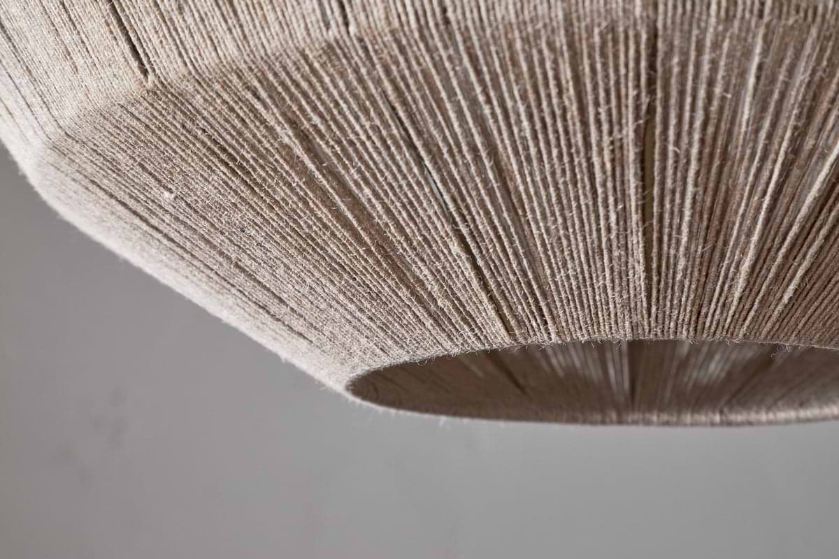 Close-up of the Nilaveli Woven Jute Sphere Pendant - Natural by nkuku, featuring a dome-shaped shade wrapped in tightly wound jute for a textured, linear pattern. The image highlights its bottom edge and surface against a soft, neutral background.