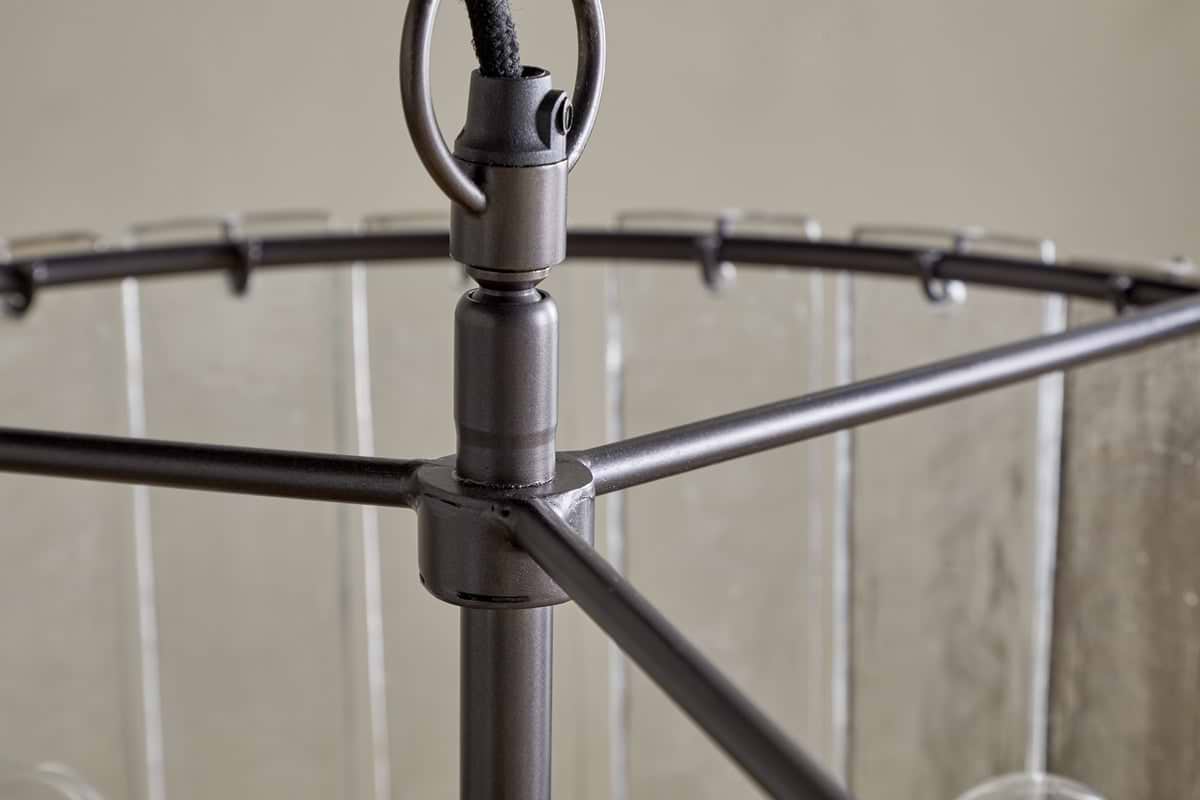 Close-up of the Nauka Statement Pendant by nkuku, featuring an aged bronze finish. The central rod links to three horizontal arms supporting a circular frame with clear glass panels, creating a refined, modern chandelier effect.