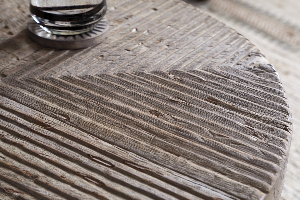 Close-up of nkuku’s Chakala Reclaimed Wood Coffee Table, featuring a chevron-patterned, textured surface with natural grooves and imperfections. A glass coaster or object is partially visible in the upper left corner.