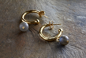 The Marai Labradorite Earrings by nkuku feature gold hoops with organic curves and a round, grayish labradorite bead drop, creating an elegant silhouette—an ideal jewelry gift.