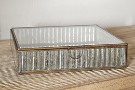 The nkuku Malita Jewellery Box features a gold-toned antique brass frame and ribbed mercury glass sides with a small metal ring pull, displayed on a light wood surface against a white wall.