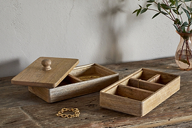 Two nkuku Chanya Mango Wood Jewellery Boxes in natural finish sit on a rustic table; one hand-carved box is open, displaying gold jewelry, while a gold bracelet and a glass vase with greenery complete the scene.