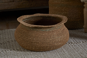 The nkuku Rana Short Basket - Natural & Moss features a handwoven round seagrass design with visible weave patterns and moss-green accents—ideal for natural home decor and pictured here on a textured, off-white rug.