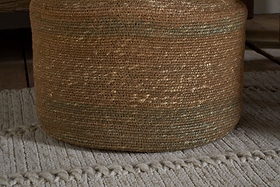 The nkuku Rana Tall Basket - Natural & Moss features subtle greenish threads and sits on a light gray, textured rug with raised lines, adding decorative storage atop wood flooring.