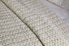 A close-up of the nkuku Peplu Cotton & Linen Screen Print Bed Quilt in sage green, showcasing Indian textile heritage with a stitched grid, tiny green florals, and subtle beige accents for timeless elegance.