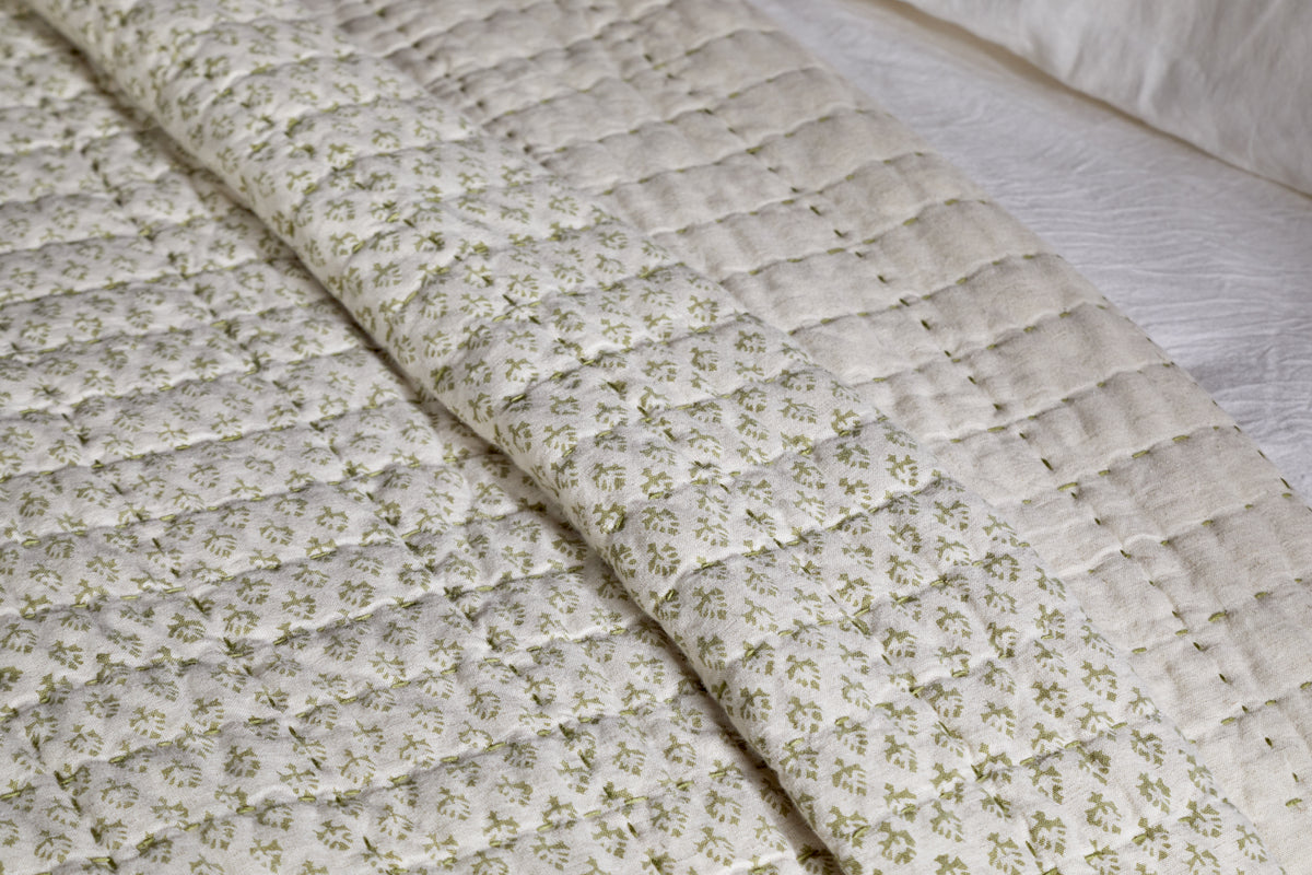 A close-up of the nkuku Peplu Cotton & Linen Screen Print Bed Quilt in sage green, showcasing Indian textile heritage with a stitched grid, tiny green florals, and subtle beige accents for timeless elegance.
