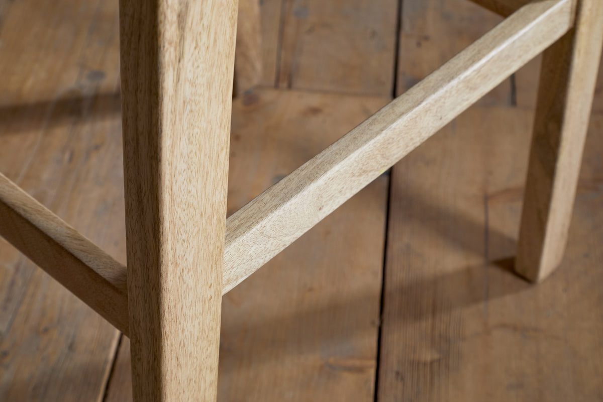 Close-up of the Aamani Mango Wood & Cord Counter Stool - Natural by nkuku, showing its light mango wood legs and support bar set on a rustic wooden floor. The image highlights the stool's smooth finish and natural color.