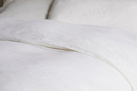 Close-up of a neatly made bed with nkuku's Cela Hemp & Cotton Duvet Cover in Natural. The sustainable, textured fabric and soft creases create a clean, cozy, and inviting atmosphere.