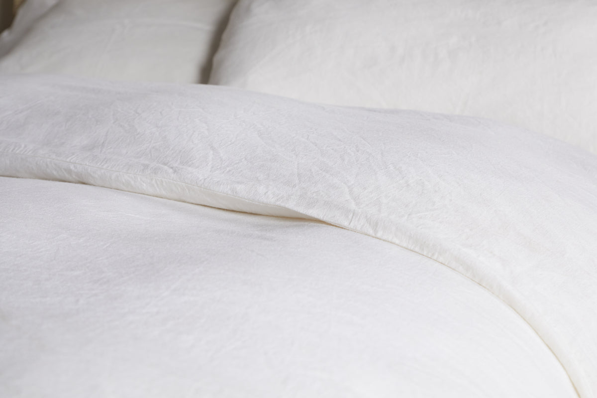 Close-up of a neatly made bed with nkuku's Cela Hemp & Cotton Duvet Cover in Natural. The sustainable, textured fabric and soft creases create a clean, cozy, and inviting atmosphere.