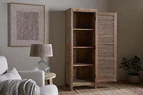 The Ibo Reclaimed Wood Slatted Tall Cabinet by nkuku stands partially open in a cozy living room with a light sofa, glass-based table lamp, framed textured artwork, a potted plant, and wooden floors.