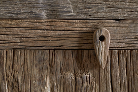 Close-up of a weathered wooden door with textured planks, featuring a tear-shaped wooden peg and dark screw—showcasing the rustic charm and natural patterns found in the nkuku Ibo Reclaimed Wood Sideboard - Natural.