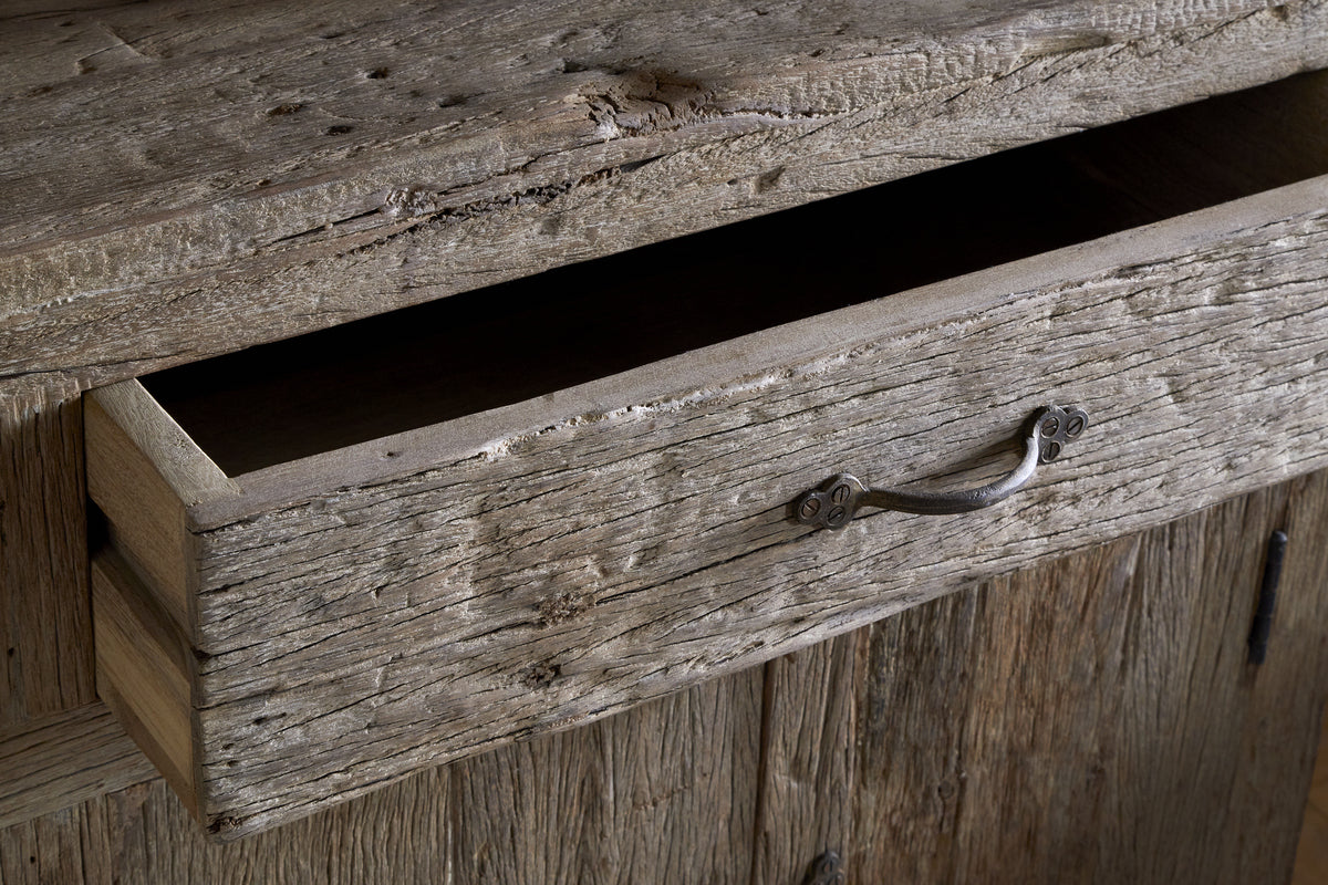 A close-up of the Ibo Reclaimed Wood Sideboard - Natural by nkuku shows its partially open drawer, rustic charm, weathered wood textures, and simple metal handle, embodying authentic sideboard style.