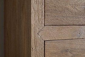 Close-up of the Iya Reclaimed Wood Tall Boy Chest of Drawers by nkuku shows precise joinery at the corner. The natural finish highlights textured grain as two panels meet with clean, mitered edges for a crisp, geometric look.