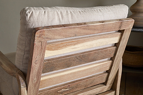 Close-up of the nkuku Jaya Acacia Wood & Linen Occasional Chair – Natural, highlighting its varied-tone horizontal acacia slats and light linen back cushion. The design creates a rustic, cozy atmosphere.