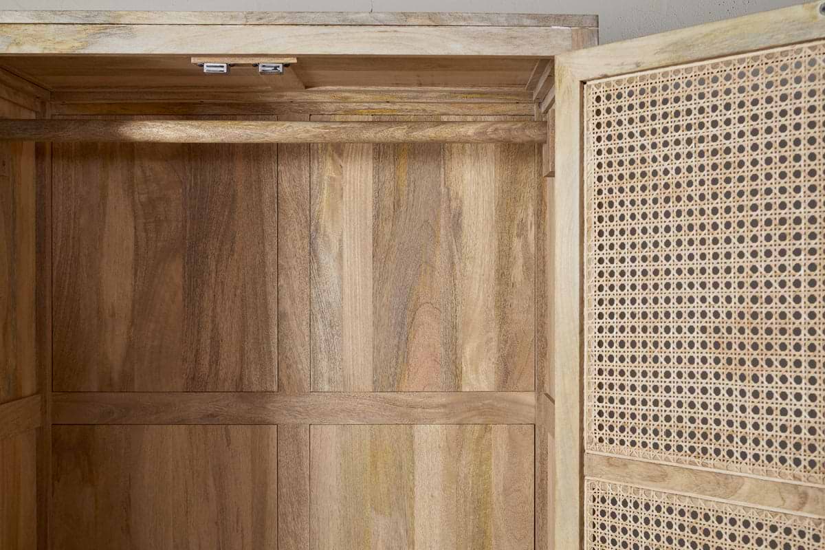 A close-up of the nkuku Kanz Mango Wood Wardrobe - Natural shows smooth, light brown mango wood panels and a door with a woven cane insert, silver hinges, and visible wood grain and texture.