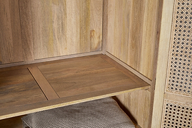 A close-up of the Kanz Mango Wood Wardrobe by nkuku showcases its natural mango wood grain shelf, woven rattan right door, and a textured light brown basket beneath, all highlighted by warm lighting.